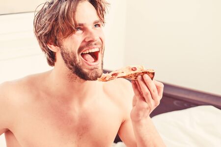 Cropped image of shirtless sexy man with pizza on bed. Man bearded handsome guy eating cheesy food for breakfast in bed. Young man resting at home with a nude and a pizza. Pizza on bed.の写真素材
