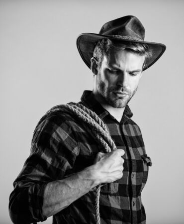 Western life. Man cowboy beige background. Man wearing hat hold rope. Ranch occupations. Lasso tool of American cowboy. Lasso is used in rodeos part competitive events. Lasso can be tied or wrappedの写真素材