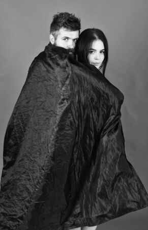 Vampire in cloak behind sexy devil girl. Man and woman dressed like vampire, demon, red background. Couple in love relations, perfect match. Girl on calm face, covered with cloak. Devil love conceの写真素材