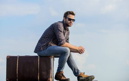 symbol of freedom. traveler wait for flight. Move. male fashion style. looking so trendy. businessman in glasses. business trip. macho man unshaven face sit on tour bag. sexy man sky backgroundの写真素材
