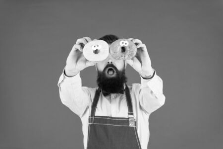 Tastiest selection of doughnuts around. Baker with glazed doughnuts. Bearded man holding ring doughnuts on red background. Hipster with baked doughnuts in handsの写真素材