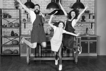 Having fun in kitchen. Family mom dad and little daughter wear aprons jump in kitchen. Family having fun cooking together. Teach kid cooking food. Weekend breakfast. Cooking with child might be funの写真素材
