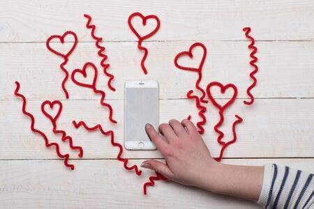 Female hand touching phone screen surrounded by fuzzy wire heartsの写真素材