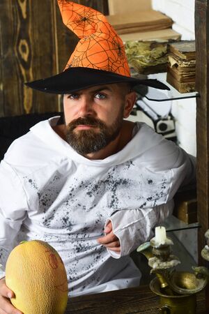 Man in orange hat with concerned face holds painted pumpkinの写真素材