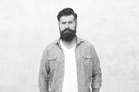 Bearded man trendy hipster style. Masculinity and male beauty concept. Hipster with beard and mustache wear denim shirt. Well groomed macho. Brutal handsome hipster man on grey wall backgroundの写真素材