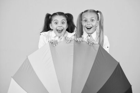 Umbrella surprise. Surprised girls hiding behind umbrela on yellow background. Little children looking with surprise. Eye opening surprise. Back to school surpriseの写真素材