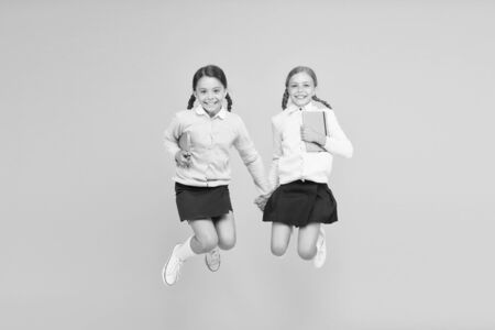Happy to be back to school. Elementary school pupils in mid air. Little girls jumping with books on yellow background. Small kids enjoying school break time. Welcome the children to schoolの写真素材