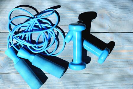 Barbells and messy skipping rope placed crosswise. Shaping and fitness equipment. Dumbbells and jump rope in cyan blue color on light wooden background, top view. Sports and healthy lifestyle conceptの写真素材