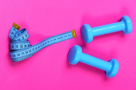 Barbells next to roll of tape measure. Dumbbells and measuring tape in cyan blue color on pink background. Shaping and fitness equipment. Healthy shape and sport conceptの写真素材