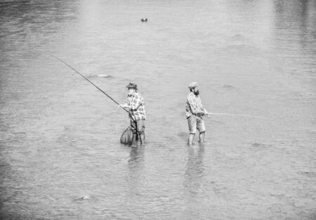 Hobby and sport activity. Fishing together. Men stand in water. Fishing is much more than fish. Male friendship. Father and son fishing. Summer weekend. Happy fisherman with fishing rod and netの写真素材