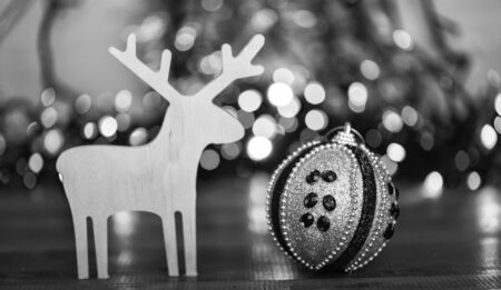 Merry Christmas concept. Ball with ornaments and wooden deer toy on blurred colorful garland background. Christmas decor. Symbols of winter holiday christmas. Deer and toy decorative ornamentの写真素材