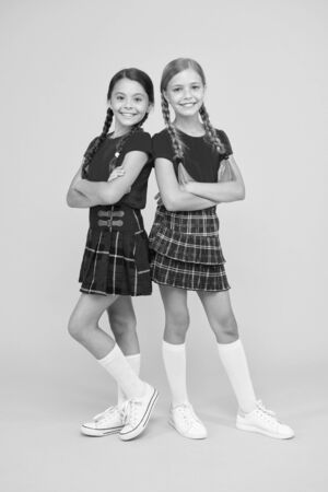 Playful kids. Happy small girls wearing same outfits. Friends enjoying friendship. Happy together. School friends having fun together. Cheerful friends. Cute little girls smiling yellow backgroundの写真素材