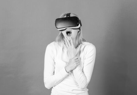 Woman wearing virtual reality goggles in blue background. Woman enjoying cyber fun experience in vr. Amazed young woman touching the air during the VR experience. Technical network.の写真素材