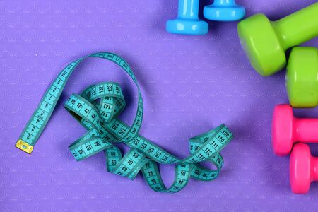 Dumbbells and measure tape in cyan color on purple textureの写真素材