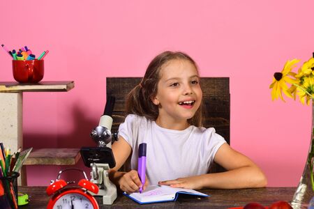 Girl sits at desk with microscope and red alarm clock