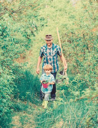 Little helper in garden. Planting flowers. Growing plants. Boy and father in nature with watering can and shovel. Dad teaching son care plants. Arbor day. Planting trees. Tree planting traditionの写真素材