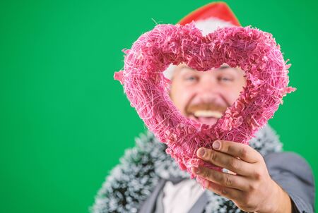 Hipster hold heart symbol of love. Bring love to family holiday. Man in love happy wear santa hat celebrate christmas green background. Spread love around. Merry christmas and happy new yearの写真素材