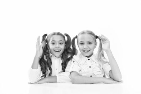 Schoolgirls sit at desk white background. Schoolgirls emotional friends. Back to school. Education concept. Beautiful girls best friends. Adorable schoolgirls. Formal style. Happy childhoodの写真素材