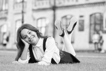 Relax at school yard. Nice time. School break for rest. Happy smiling pupil. Girl cute kid laying green grass. Happy kid relaxing outdoors. Girl school uniform enjoy relax. Cheerful schoolgirlの写真素材