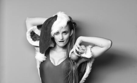 Sexy christmas costumes. Santa girl sexy with make up. Woman attractive santa celebrate new year. Girl red swimsuit and santa hat hold christmas ball decoration. Santa girl christmas party masqueradeの写真素材
