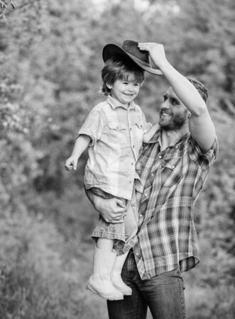 Child having fun cowboy dad. Farm family. Holidays at parents farm. Growing cute cowboy. Weekend at farm. Little boy and father in nature background. Spirit of adventures. Little helper in gardenの写真素材