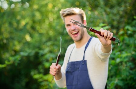Man hold barbeque equipment. Grilling food. Barbecue utensils. Summer weekend. Tools for roasting meat outdoors. Barbeque party. Cooking burgers. Picnic concept. Bbq chef. Handsome guy cooking foodの写真素材