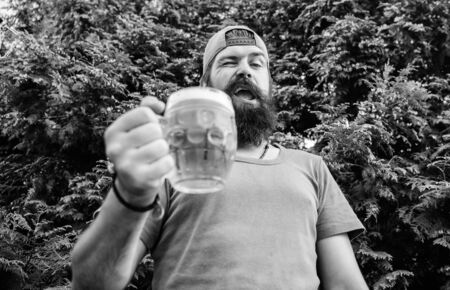 In playful mood. Brutal hipster with winking face having craft beer. Man drinker holding beer mug. Bearded man enjoy drinking beer on nature. Fun loving beerの写真素材