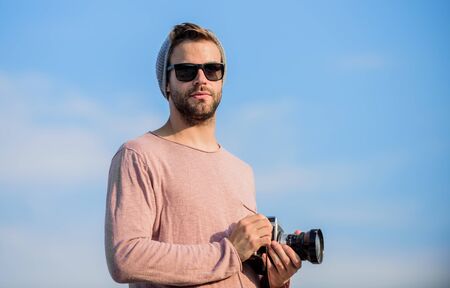 Photojournalist concept. Travel blogger. Professional photographer. Hipster reporter taking photo. Guy photographer outdoors sky background. Handsome photographer guy retro camera. Manual settingsの写真素材