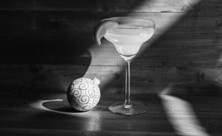 Alcohol cocktail margarita with piece of orange near christmas ball ornament on dark blue background. Celebrate new year cocktail. Bar winter season cocktail menu. Winter cocktail drink conceptの写真素材