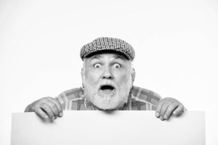 Elderly person. Announcement concept. Event announcement. Senior bearded emotional man peek out of banner place announcement. Pensioner grandfather in vintage hat poster information copy spaceの写真素材