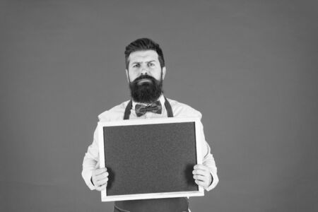 urgent to eat. Food blogger. serious hipster bartender. What to cook. Restaurant menu. cafe shop advertisement. bearded man chalkboard, copy space. brutal waiter in kitchen. mature man red backgroundの写真素材