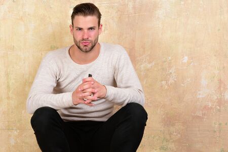 Guy with beard holds phone. Macho sits on beige backgroundの写真素材