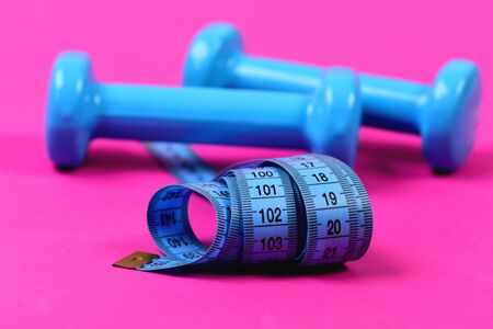 Barbells next to roll of tape measure. Dumbbells and measuring tape in cyan blue color on defocused...