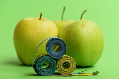 Pattern made of apple fruits near blue and yellow tape measures. Apples near measuring tape rolls on green background, close up. Sports and healthy lifestyle symbols. Athletics and weight loss conceptの写真素材
