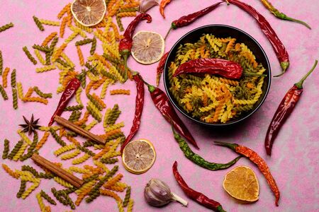 delicious colorful Italian pasta in ceramic plate with spoon , chili pepper, orange, garlic, star anise and cinnamon on pink textured background, copy spaceの写真素材