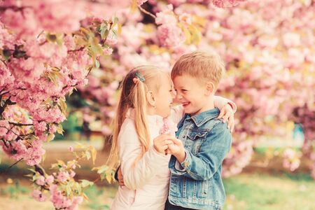 Tender love feelings. Couple kids on flowers of sakura tree background. Little girl enjoy spring flowers. Giving all flowers to her. Surprising her. Kids enjoying pink cherry blossom. Romantic babiesの写真素材