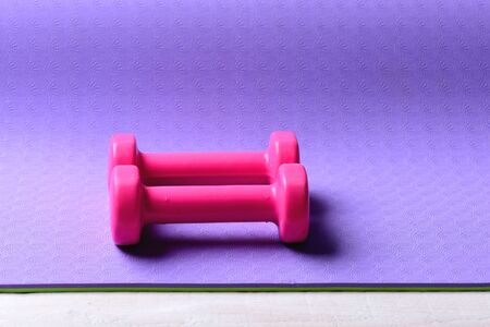 Shaping and fitness equipment. Healthy shape and sport concept. Dumbbells made of pink plastic on purple texture background. Barbells in small size, close up and copy spaceの写真素材
