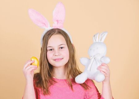 Origin of easter bunny. Easter symbols and traditions. Playful child with soft toy. Meet spring holiday. Easter egg hunts as part of festival. Girl little child easter bunny accessory hold dyed eggの写真素材