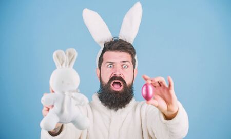 Bearded man wear bunny ears. Egg hunt. Look what i found. Hipster cute bunny blue background. Easter bunny. My precious. Funny bunny with beard and mustache hold pink egg. Easter symbol conceptの写真素材