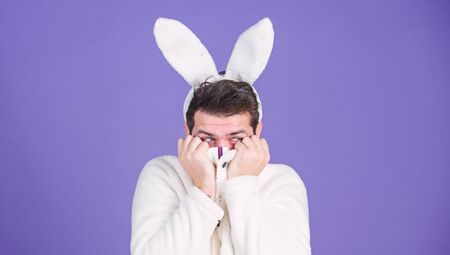 White bunny symbol of easter holiday. Soft and tender. Guy with long bunny or rabbit ears on violet background. Enjoy tenderness. Cute bunny. Man handsome face wear white bunny ears. Easter bunnyの写真素材
