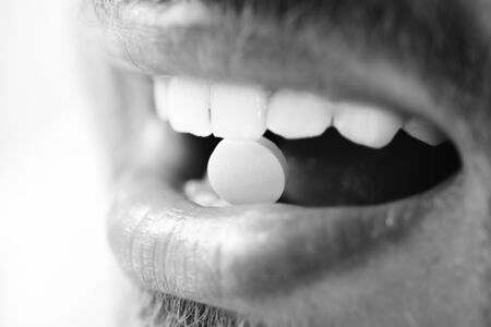 Guys mouth with round pink drug, close up. Medical treatment or health concept. Patients teeth hold pill in his teeth isolated on white background, selective focusの写真素材