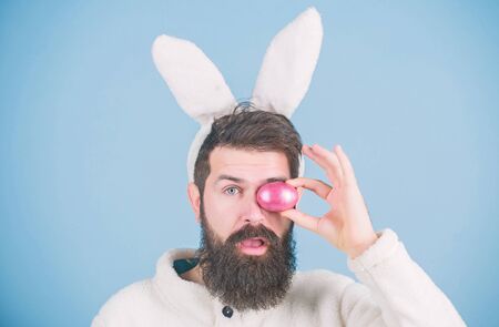 Having fun. Funny bunny with beard and mustache hold pink egg. Bearded man wear silly bunny ears. Easter symbol concept. My precious. Hipster cute bunny long ears blue background. Easter bunnyの写真素材