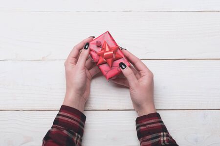 Female hands hold box wrapped in red paper with bowの写真素材