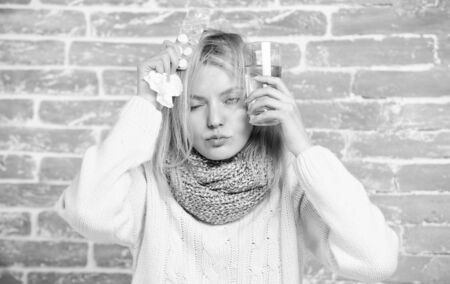 Suffering from pain. Ill woman treating symptoms caused by cold or flu. Cute sick girl taking anti cold pills. Unhealthy woman holding pills and water glass. Medication and increased fluid intakeの写真素材