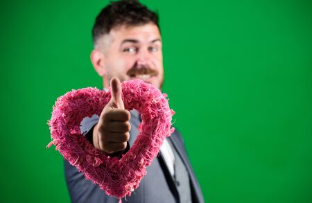 Romantic macho flirting. Happy valentines day. Hipster hold heart symbol love. Man formal suit celebrate valentines day green background. Spread love around. Happy in love. Hey prettyの写真素材