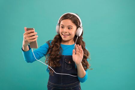 hello. kid long hair make selfie in headset. small child make play list on smartphone. small girl...