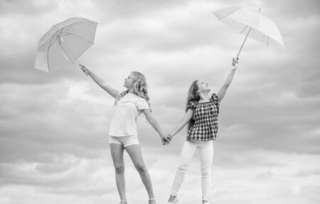 Carefree children outdoors. Girls friends with umbrellas cloudy sky background. Ready for any weather. Windy or rainy we are prepared. Freedom and freshness. Weather forecast. Weather changingの写真素材