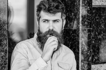 Bearded brutal male smoking electronic cigarette. Mature hipster with beard. Health safety...