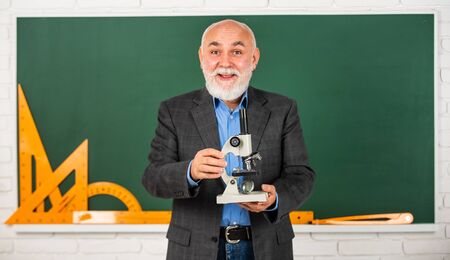 happy senior teacher use microscope. chemistry in school laboratory. science experiments with microscope in lab. Biology school laboratory equipment. man in classroom with math tools at blackboardの写真素材