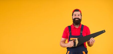 Sharp blade of saw. Dangerous job. Feeling manly. Carpenter with saw in hands. Masculinity concept. Handsome man with saw yellow background. Gardener lumberjack equipment. Tools shop copy spaceの写真素材